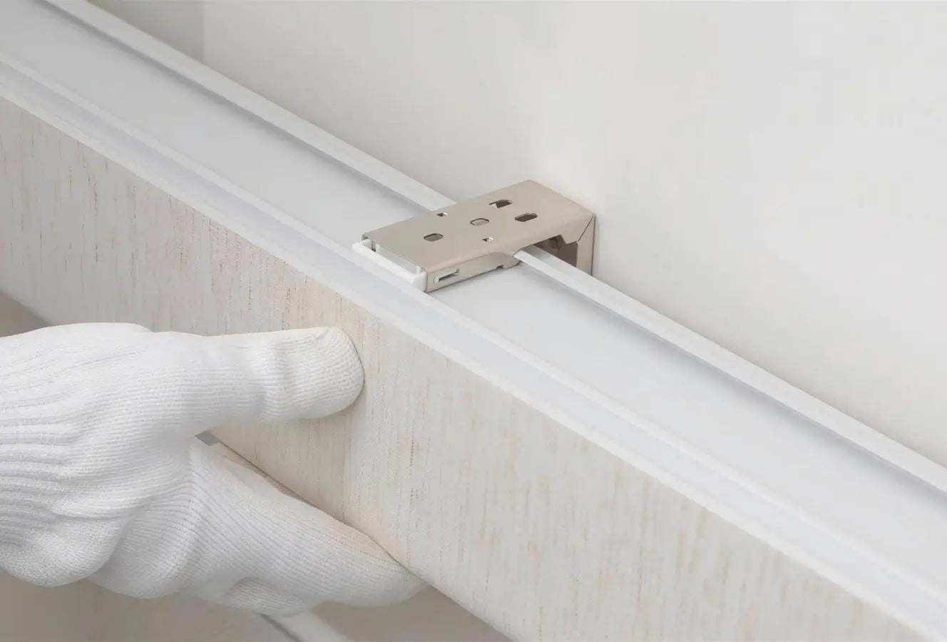 Hand wearing a white glove adjusting a metal bracket on a white strip of material.