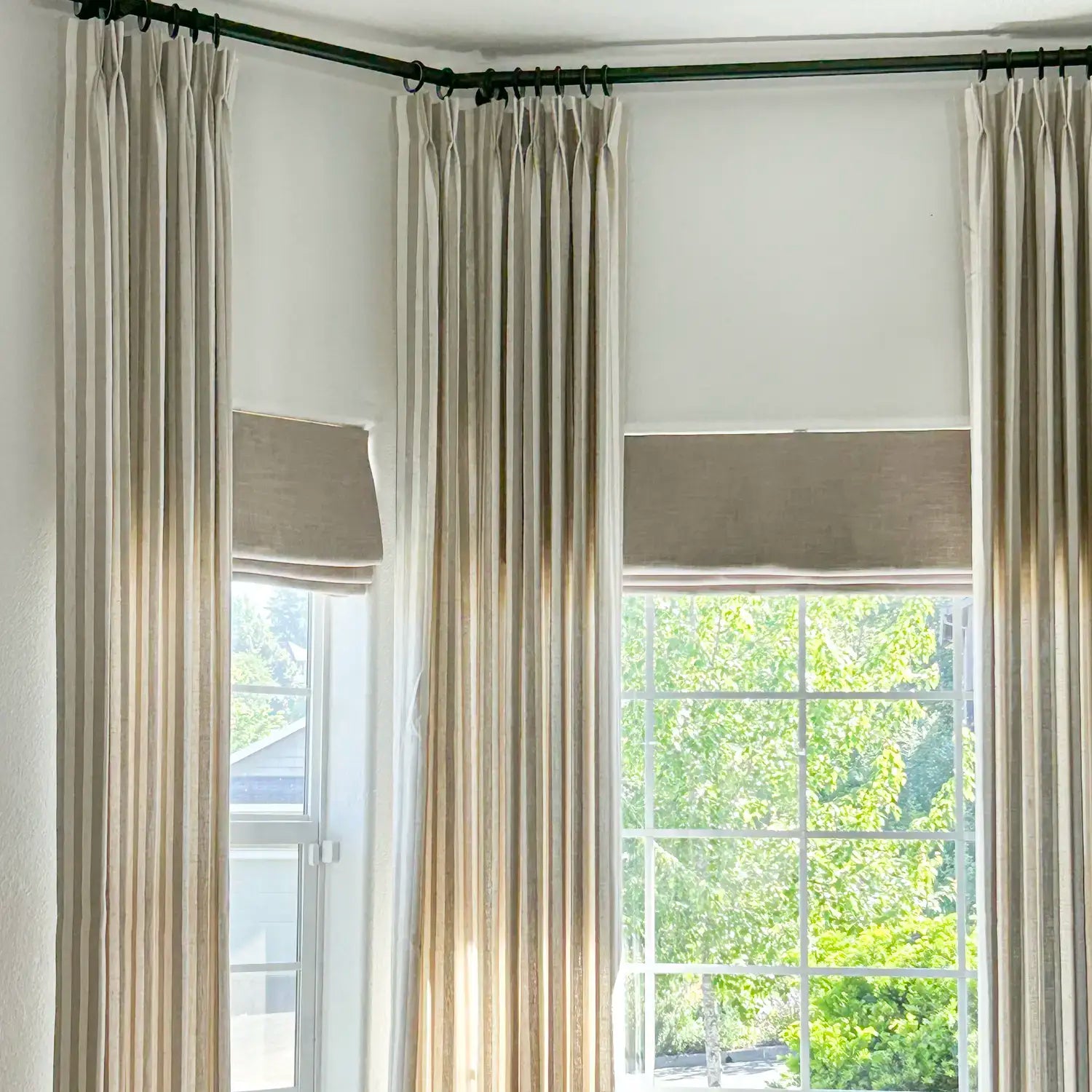 Beige curtains with window treatments in a room with a view of trees outside.