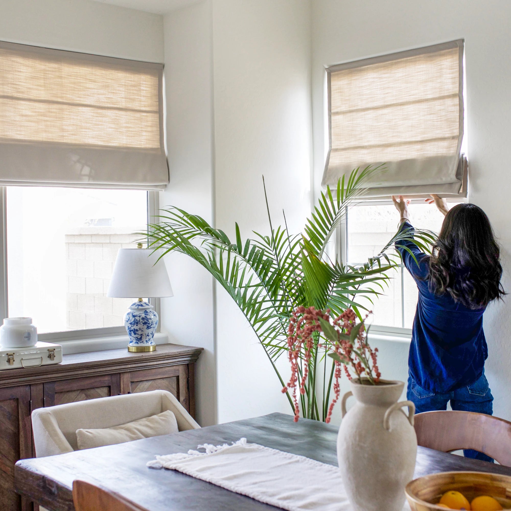 Ilythra cotton linen roman shades in a dining room view 3 featuring a hand adjusting the shades