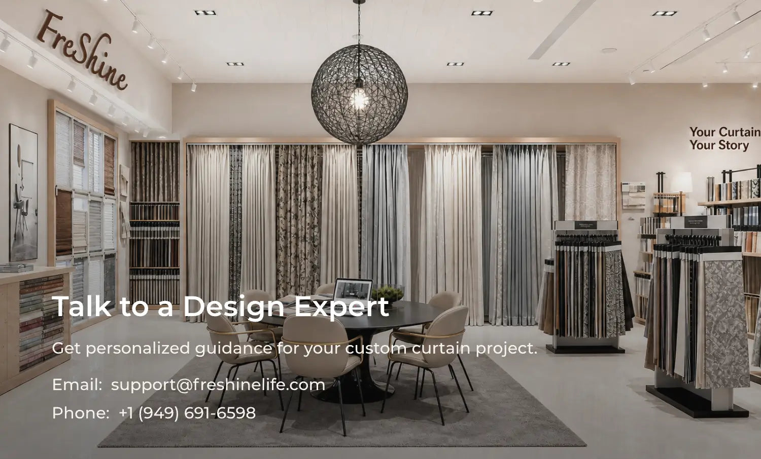 A modern interior showroom with a round dining table and six upholstered chairs placed on a gray rug in front of large curtain samples. The room has bright lighting, a black spherical pendant light, wall-mounted display cases, and fabric sample racks.