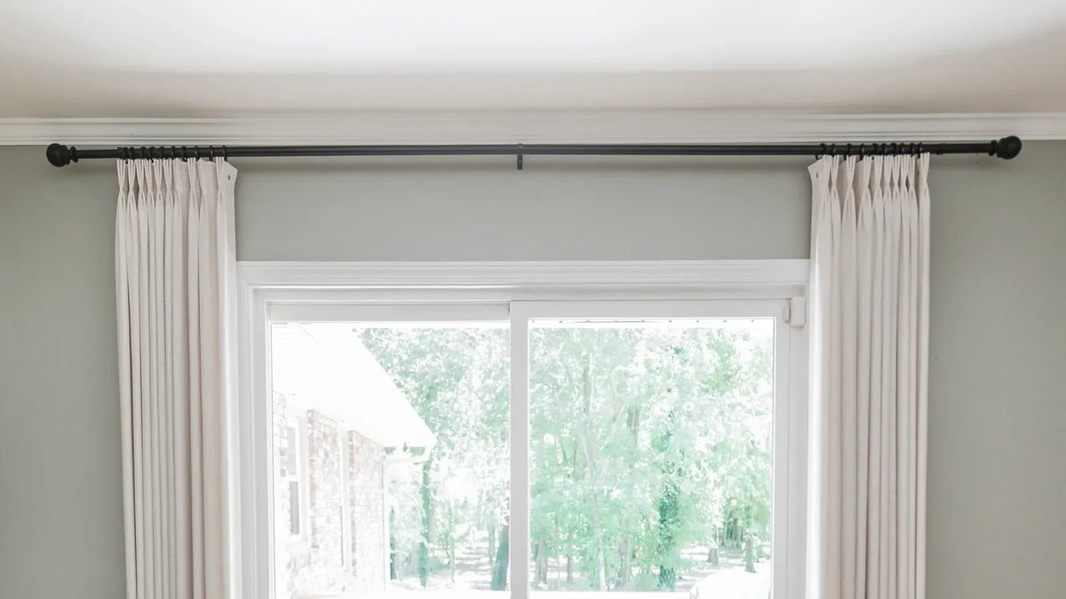 Pinch-pleated panels on a black rod run well past a sliding glass door, so the open curtains stack clear of the opening