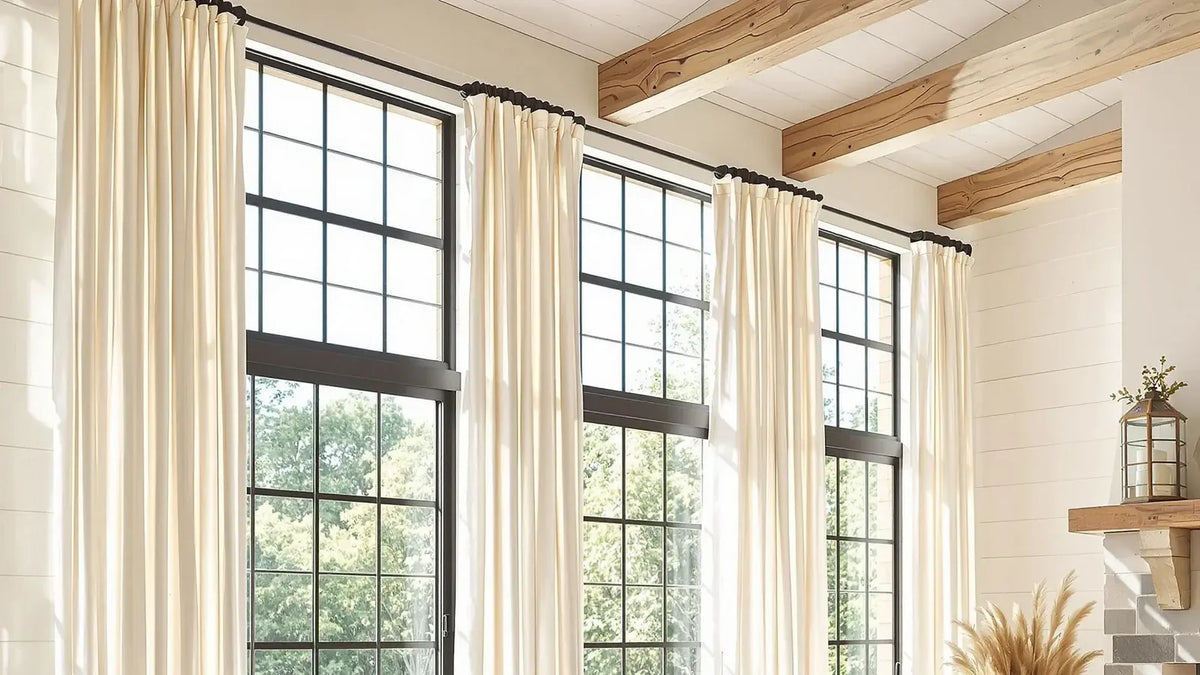 Extra-long cream linen-blend drapes on black rods across tall windows in a double-height living room