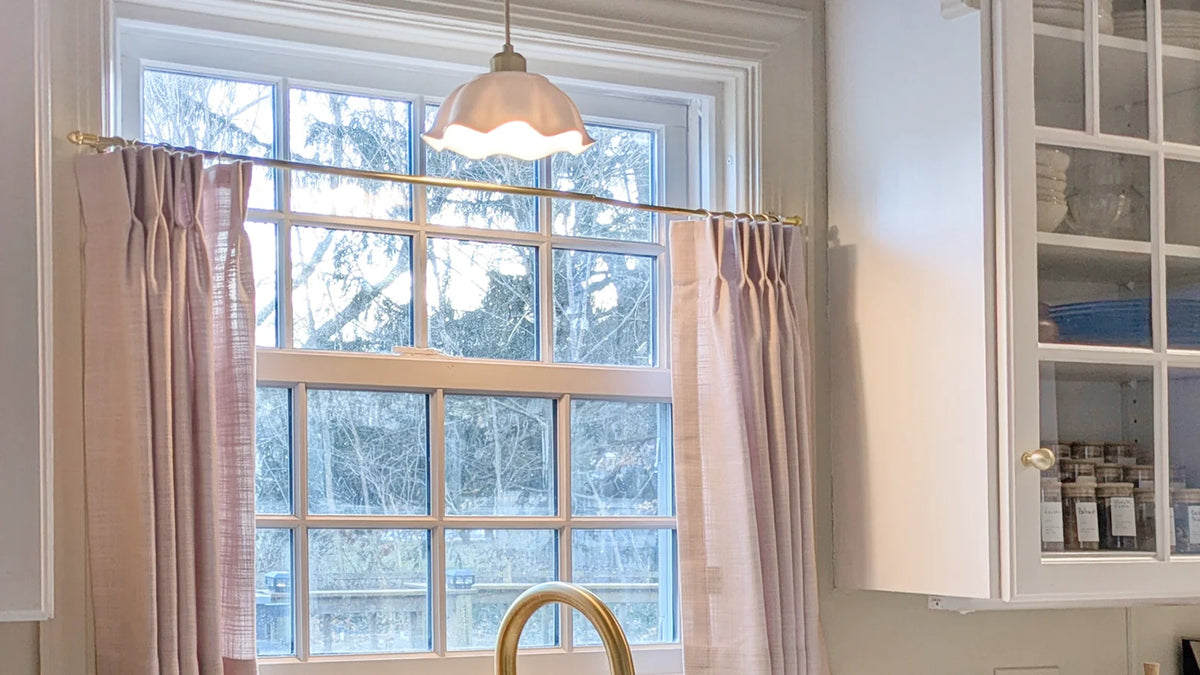 Pinch-pleated linen-blend café curtains on a brass rod over a kitchen sink window