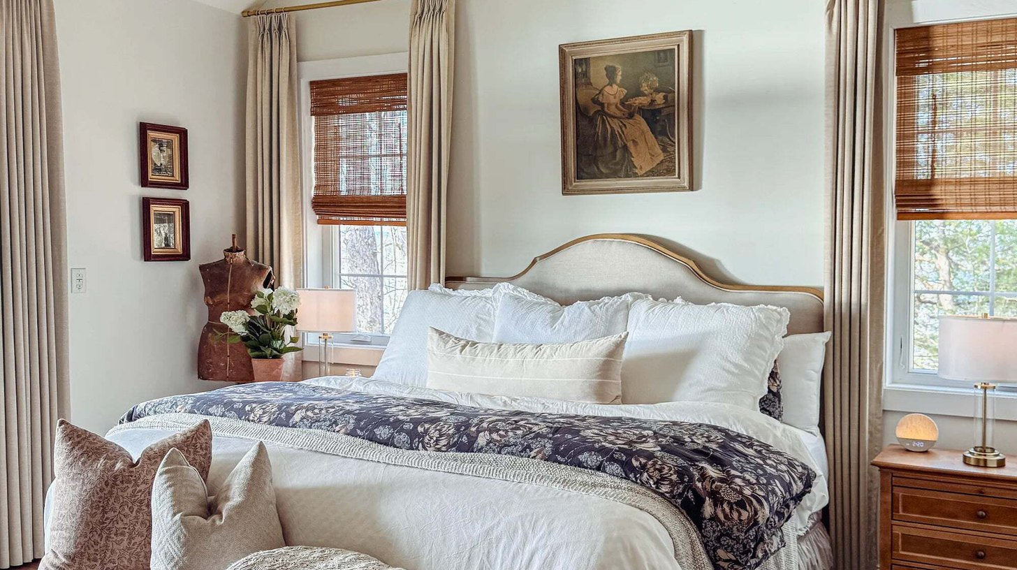 Bedroom with linen curtains on brass rods layered over woven shades at three windows
