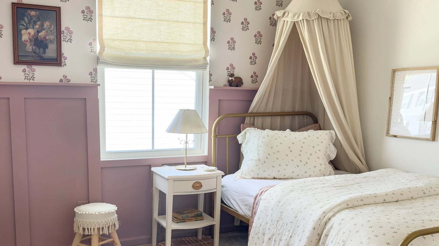 Girl's bedroom with a soft Roman shade at the window, floral wallpaper and a brass bed