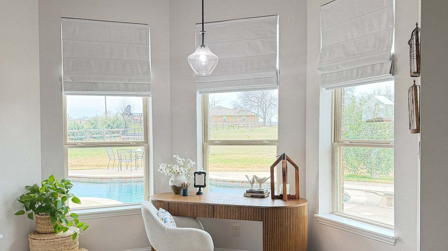 Three motorized linen Roman shades raised to different heights across a bedroom bay window
