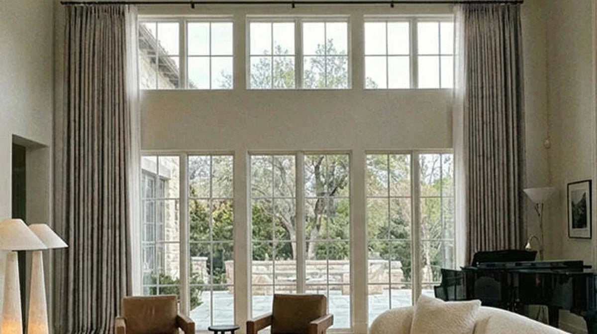 Floor-to-ceiling lined curtains framing a two-storey wall of glass in a living room