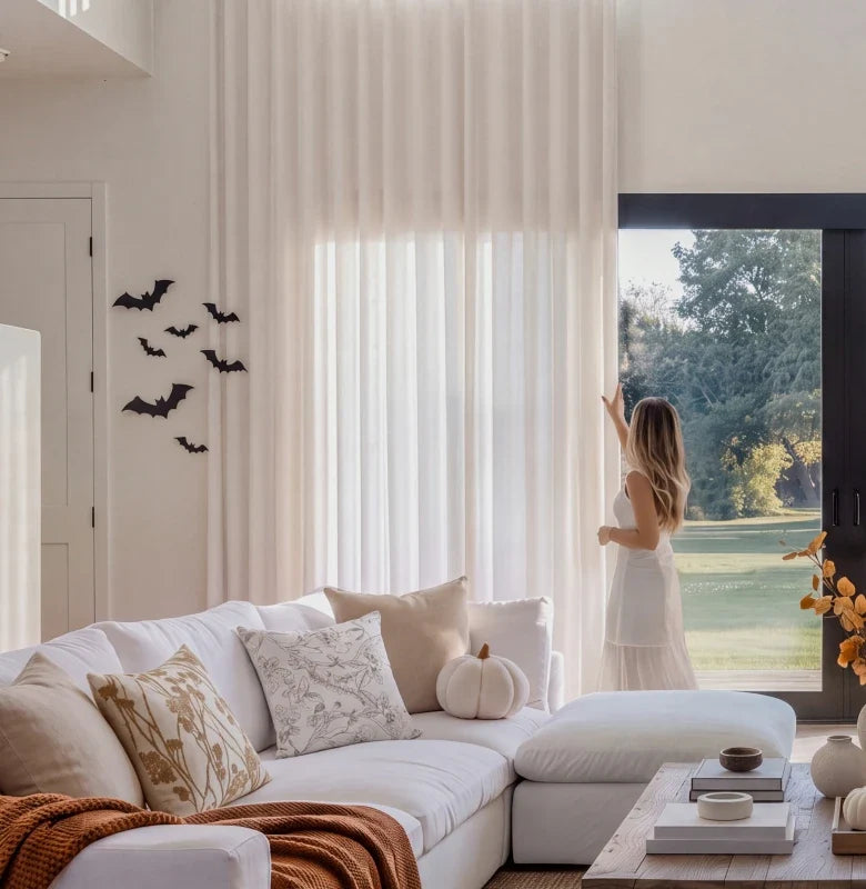 Sheer curtains and a sofa beside a window, with Halloween bats and pumpkins.