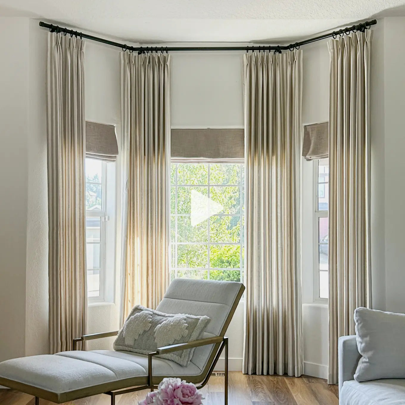 Translation missing: en.A set of floor-length beige curtains with matching window valances styled in a bright, modern living room featuring a curved bay window, a light gray chaise lounge, and wood flooring