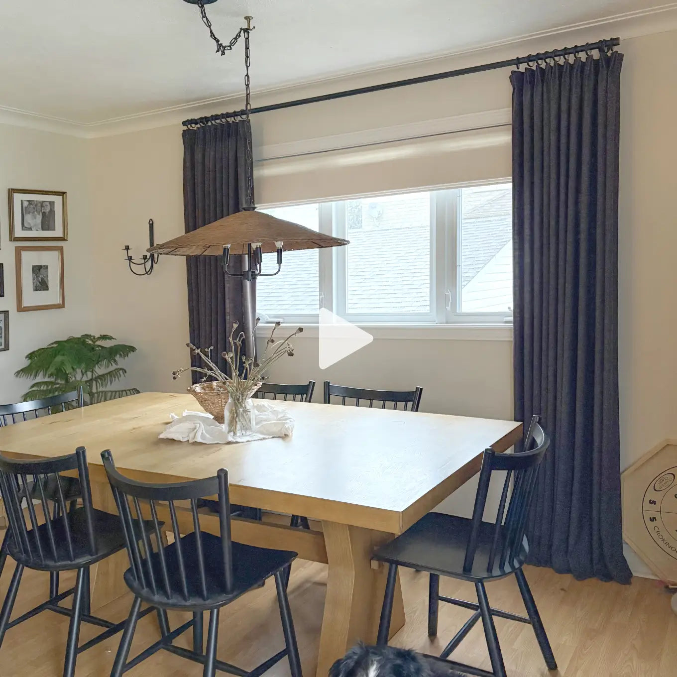 Translation missing: en.A dining room scene with a light wood rectangular table, black spindle-back chairs, dark charcoal gray curtains, a hanging pendant light, and a window in the background