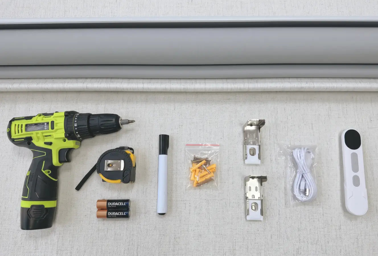 Tools and hardware items including a drill, batteries, tape measure, marker, screws, and clips on a textured surface.